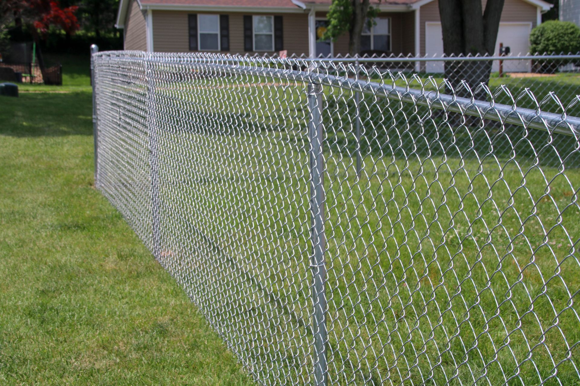 Chain-link fence in front yard of a house with green grass.