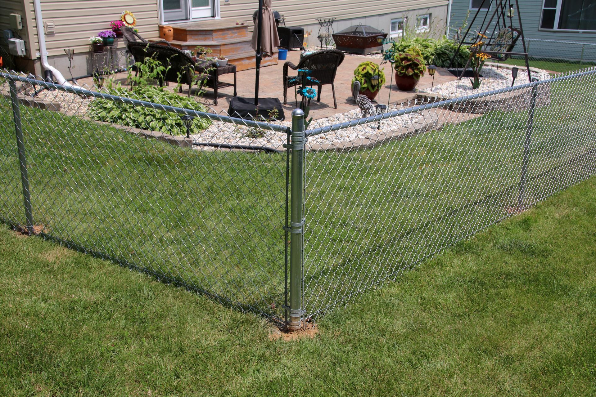 Chain-link fence surrounds a patio with lawn in the foreground. Sunlight illuminates the scene.