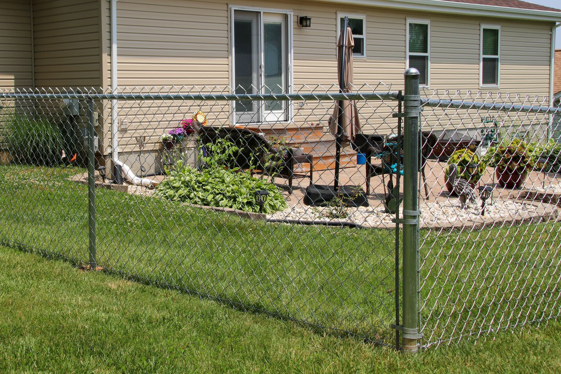 Green chain-link fence in front of a house with a patio and sliding glass door.