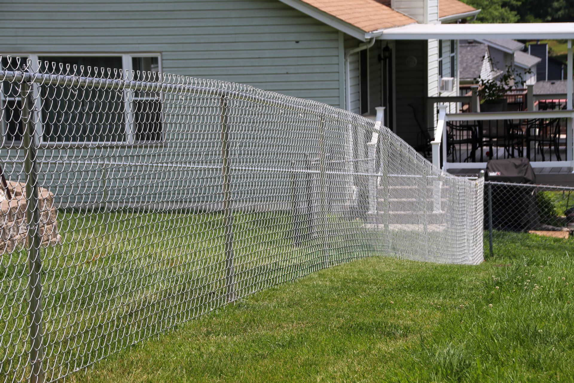 Chain-link fence in front of a house, with green grass in yard.