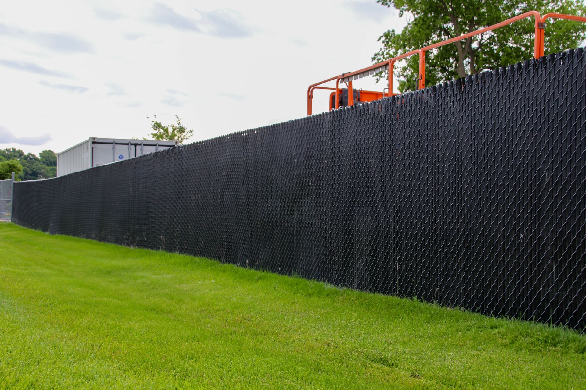 Black privacy fence along a grassy area, with an orange lift visible above.