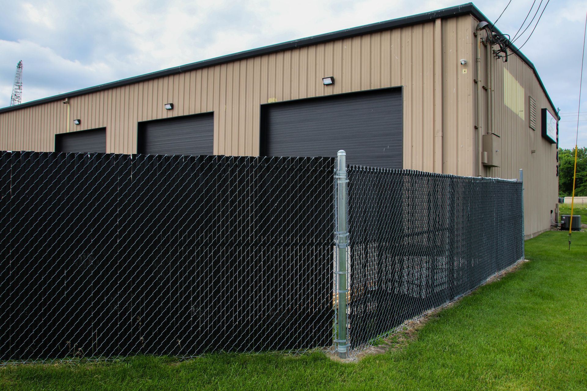 Black chain-link fence in front of a tan metal building with three closed garage doors.