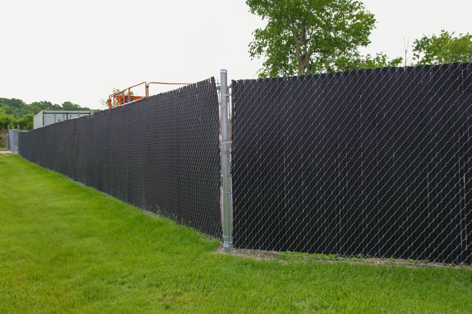 Black privacy slats in chain-link fence on green grass. Metal post on the right.