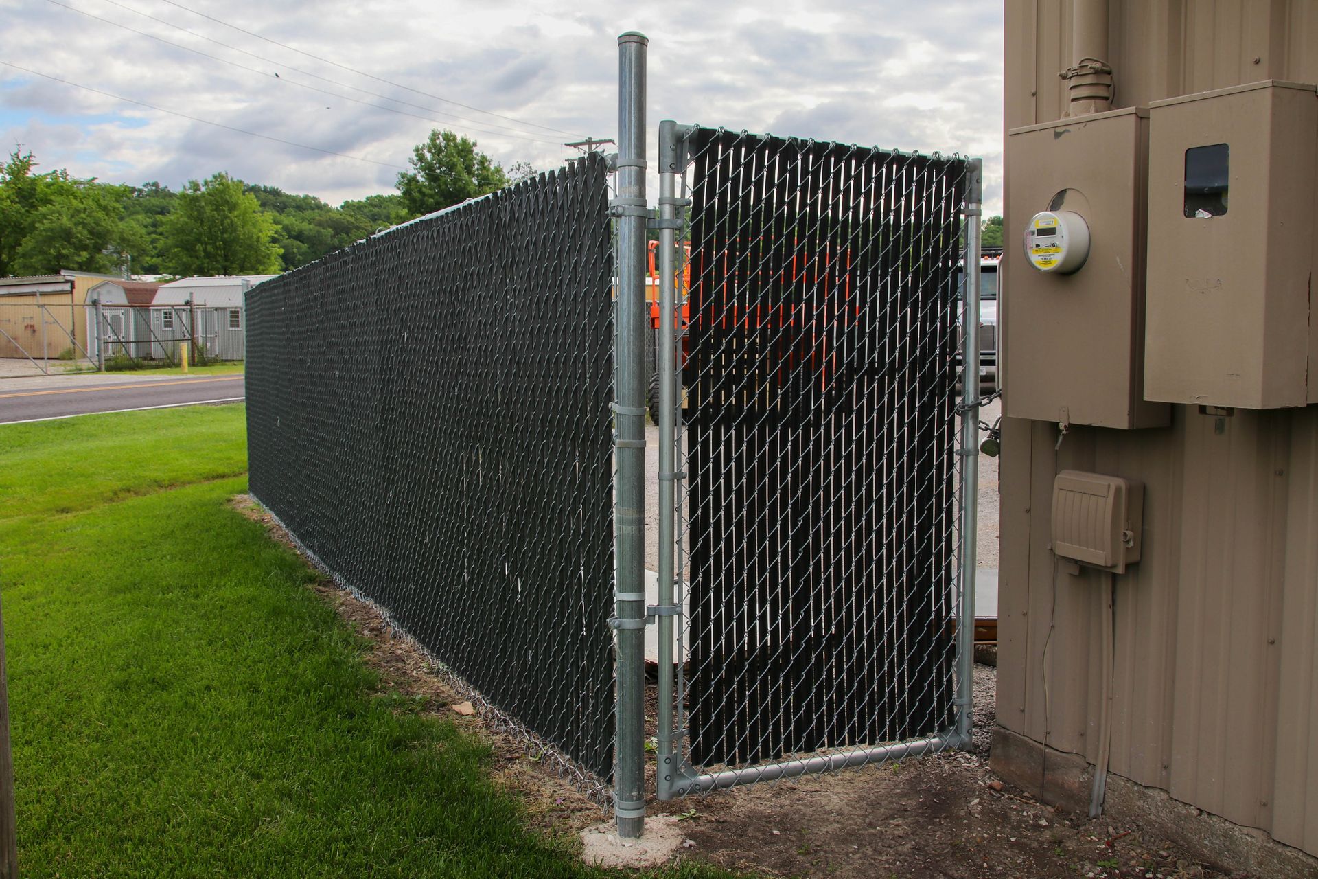 Black chain link fence with privacy slats, bordering a grassy area and building exterior.