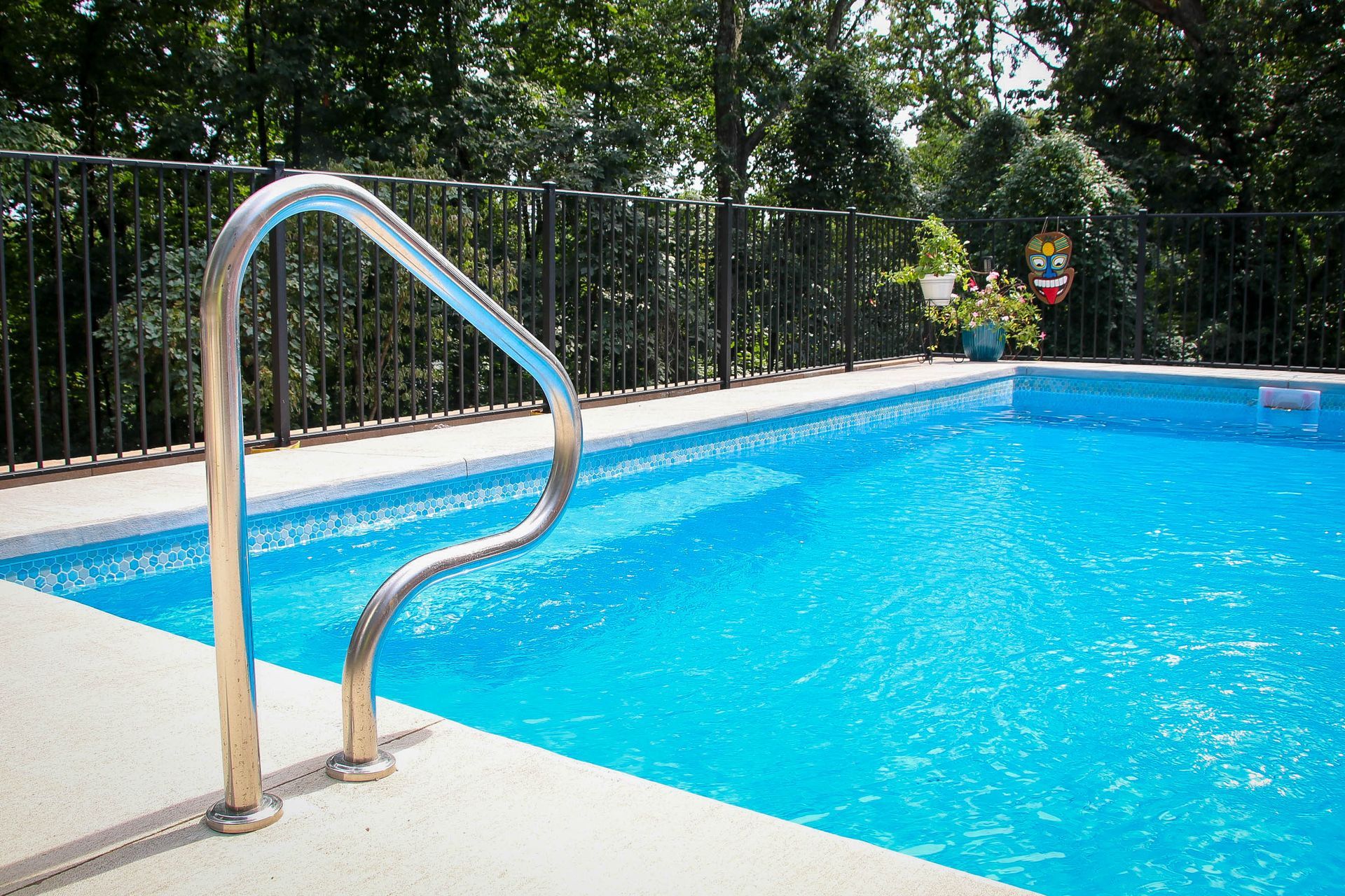 Swimming pool with a stainless steel handrail, surrounded by a black fence and trees.