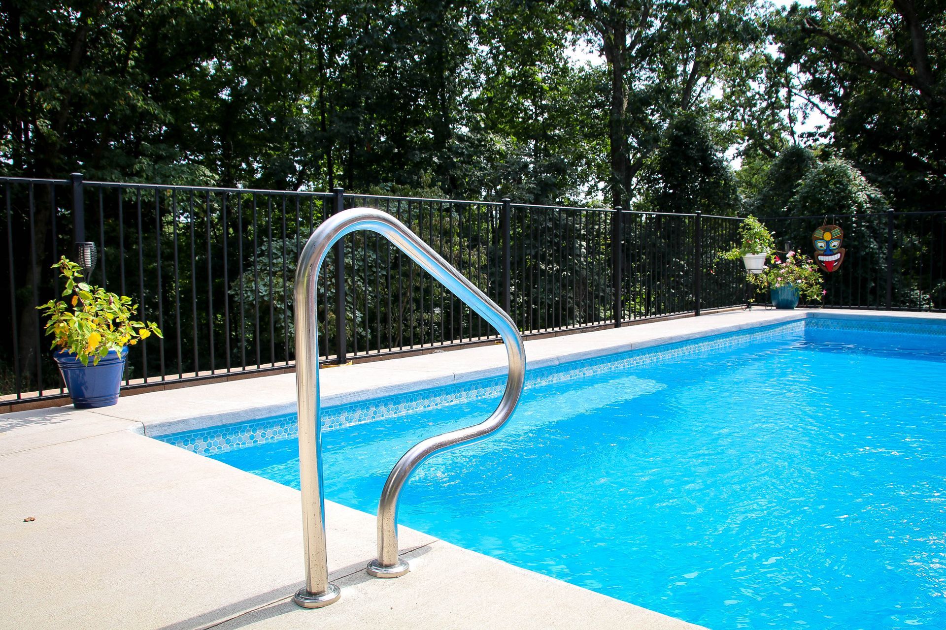 Swimming pool with blue water, chrome handrail, and black fence.