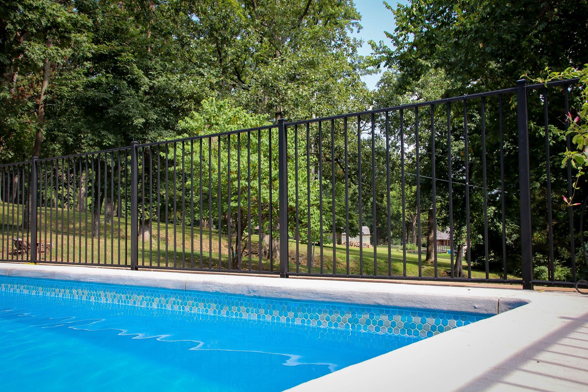 Black metal fence surrounds a blue swimming pool, with trees in the background.