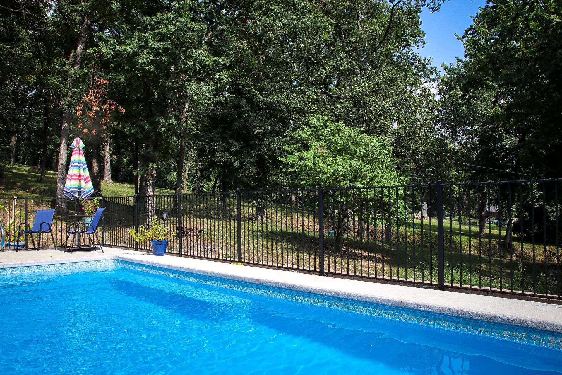 Swimming pool with a black fence, trees, and patio furniture.