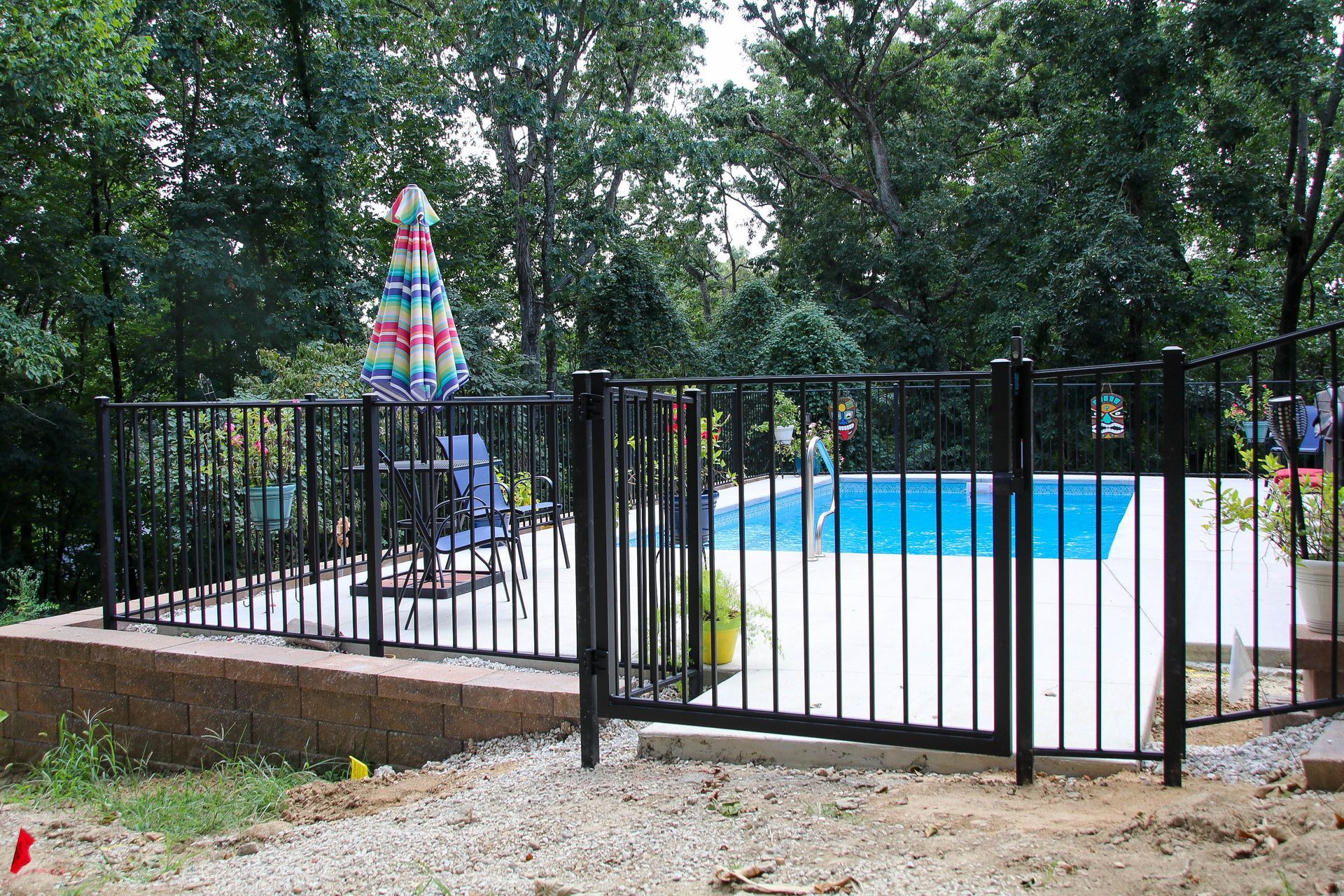 Black metal fence surrounds a small pool on a concrete patio, with trees in the background.
