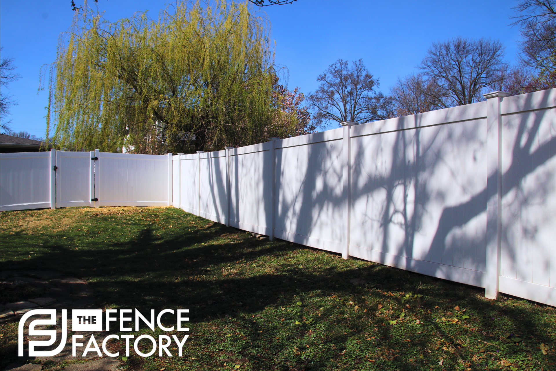 White vinyl fence in a grassy backyard, under a sunny sky.