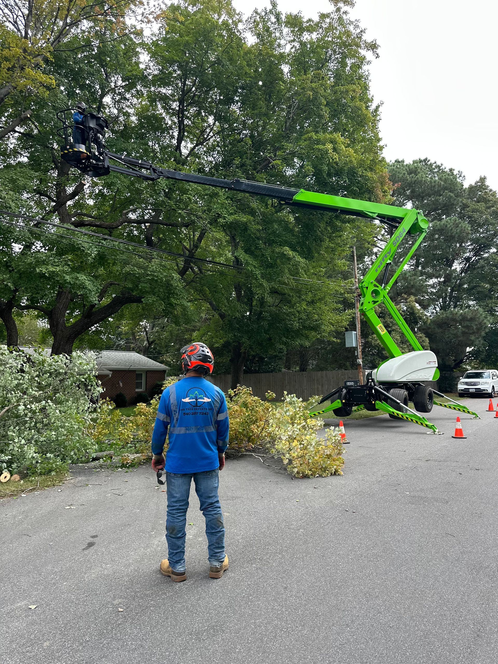 Man watches a green lift trimming a tree in a residential area. Cut branches on the ground.