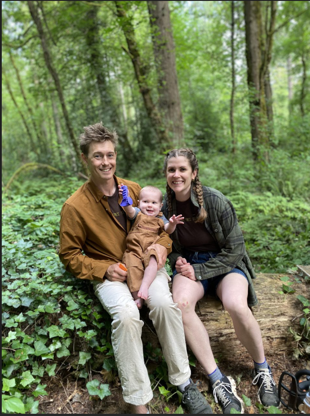 Three people sitting on a log in a lush green forest, smiling at the camera.