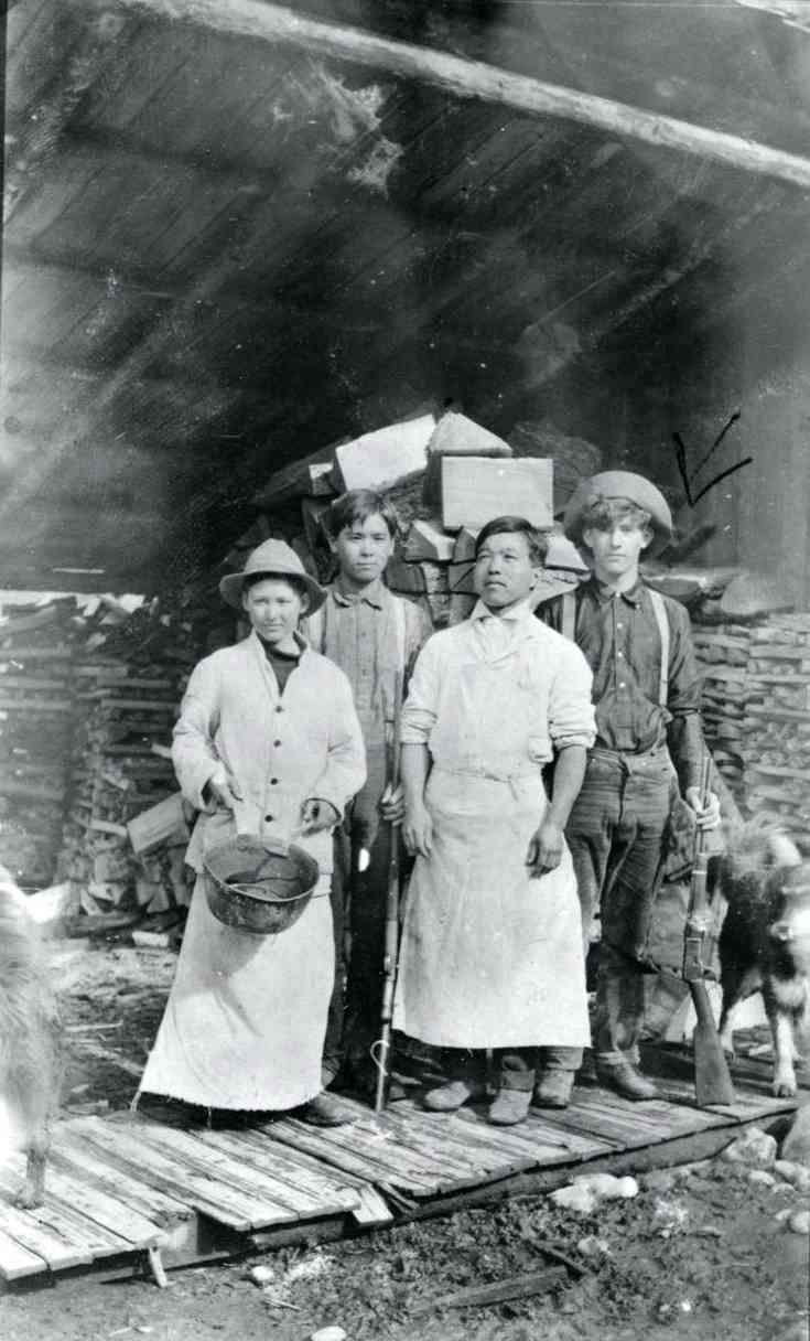Four people standing in front of a cave entrance with mining equipment and supplies.