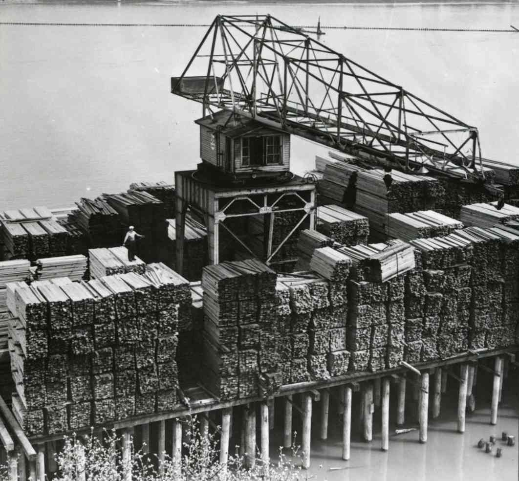 Black-and-white photo of a large industrial crane atop a stacked construction site on pilings