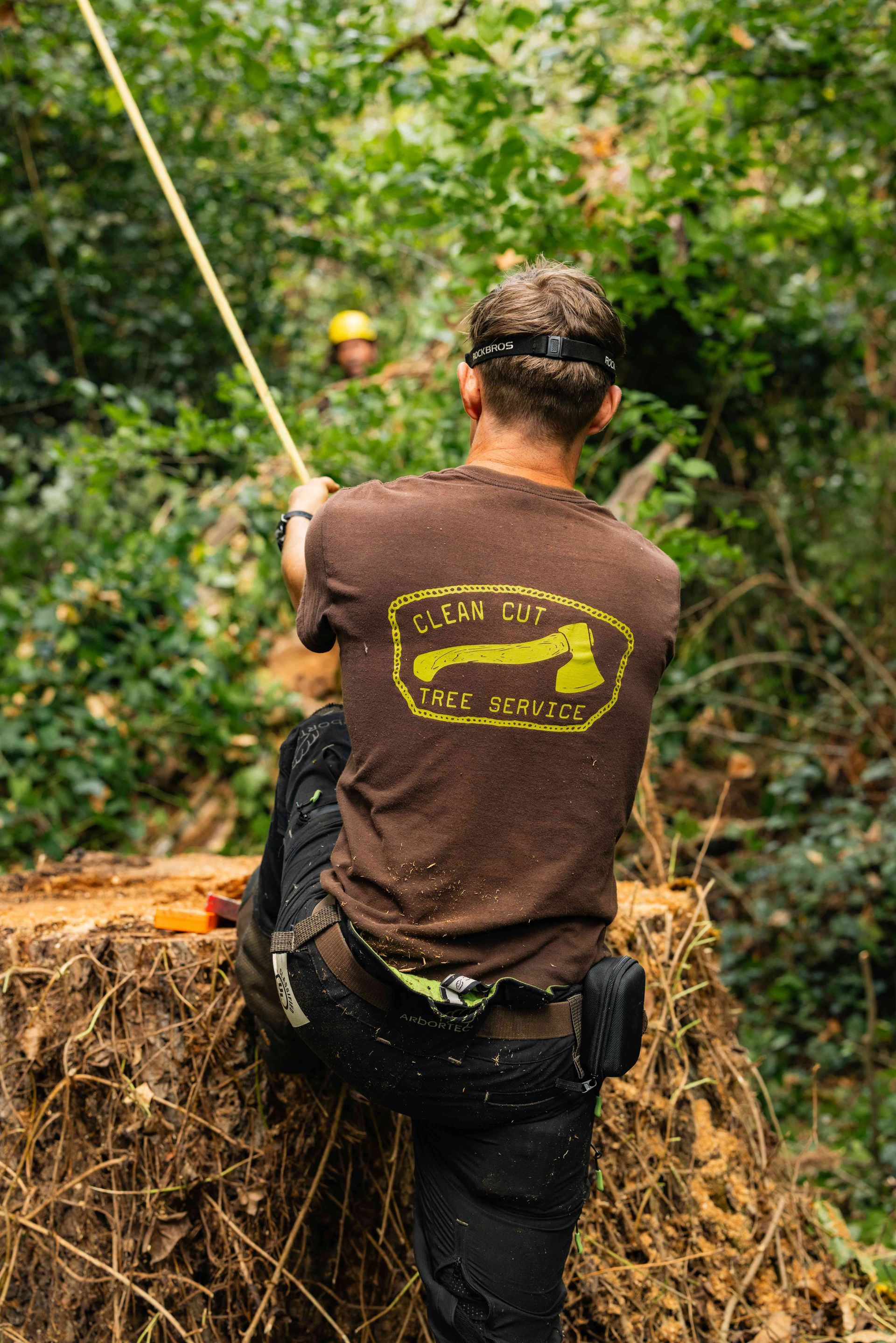 Worker in brown shirt using a rope on a hay bale platform in a wooded area