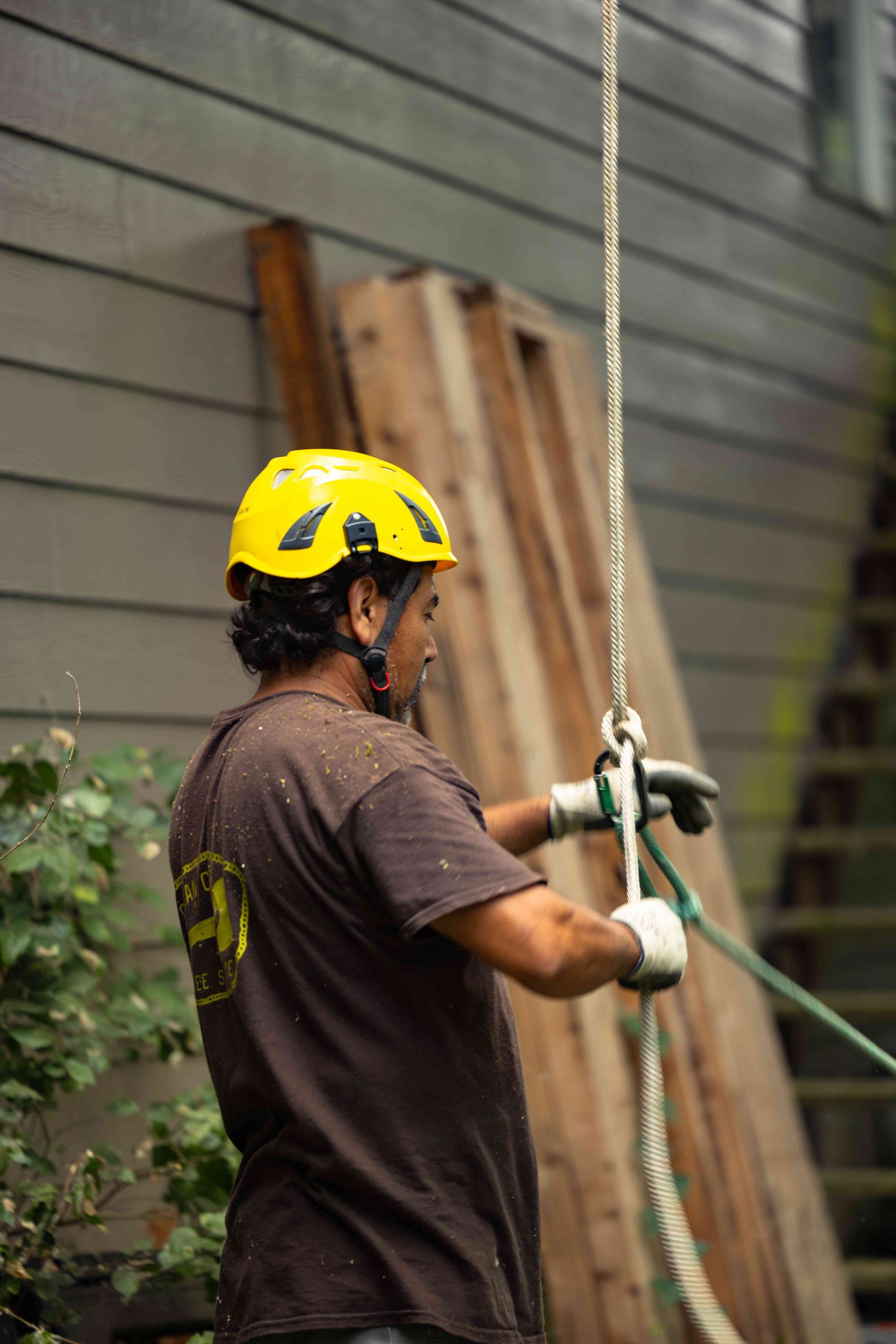 Worker in yellow helmet operating a rope tool beside a house exterior