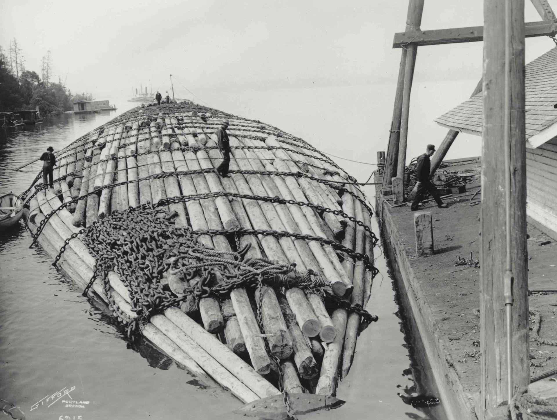 Workers shaping a large curved structure with logs and wire mesh beside a waterfront
