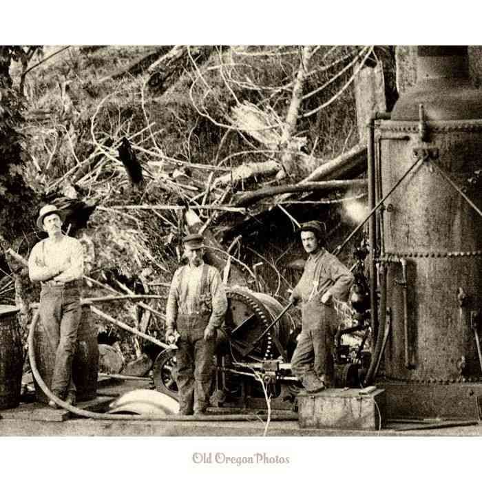 Three men stand beside mining machinery in a wooded area, with pipes and equipment in the background.