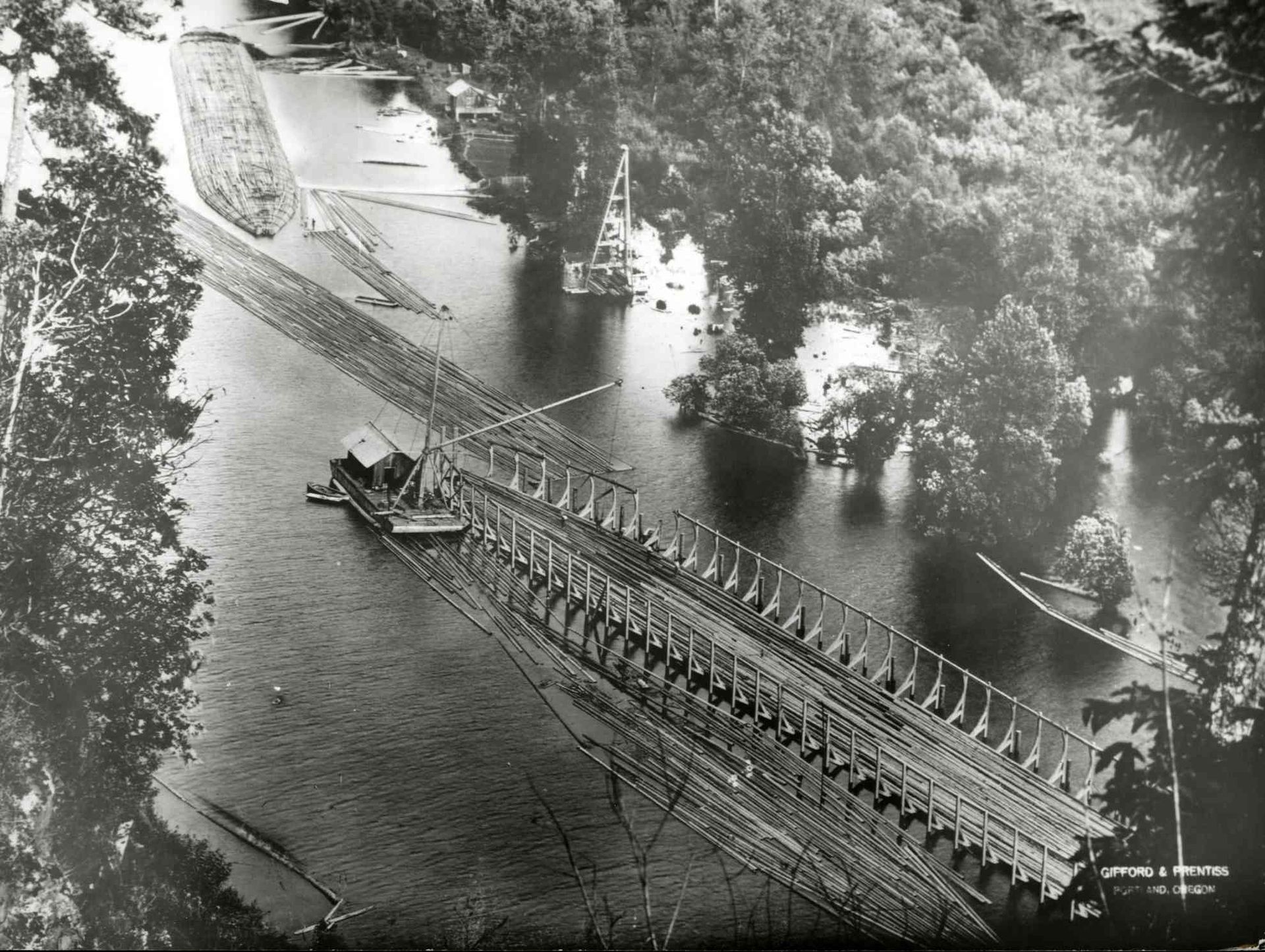 Aerial view of a long bridge spanning a river beside a wooded shoreline and small boat