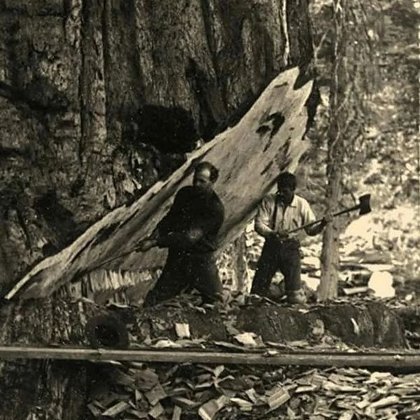 Two people standing by a wooden canoe in a rocky forest clearing