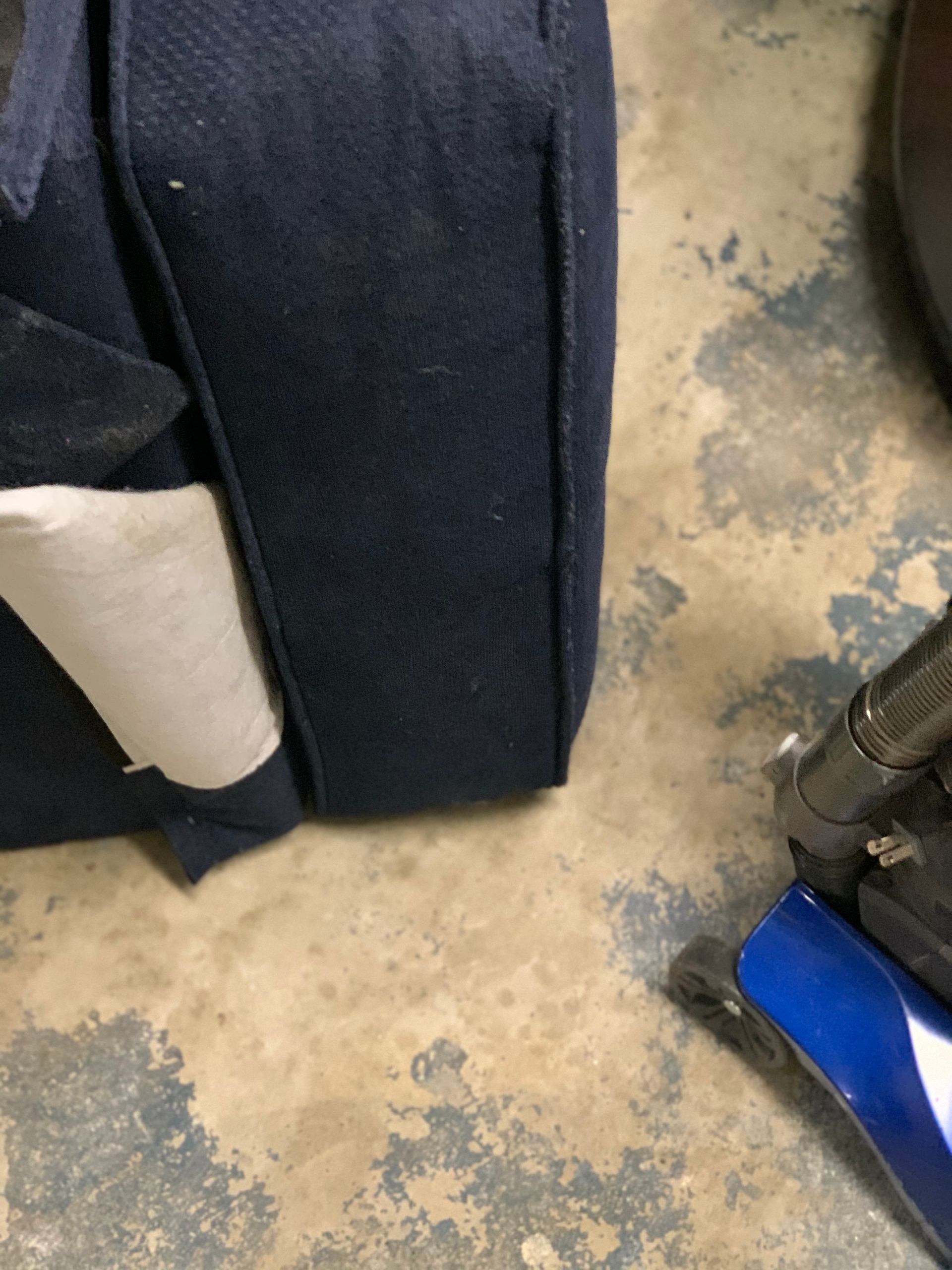 A blue bag is sitting on a concrete floor next to a vacuum cleaner.