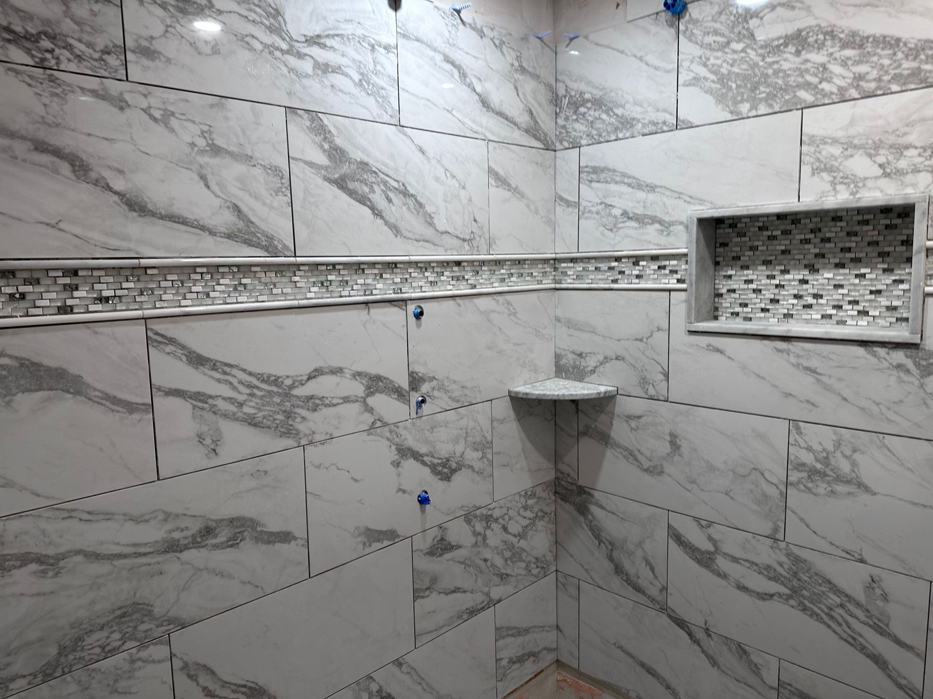 A bathroom with marble tiles and a shelf in the shower.
