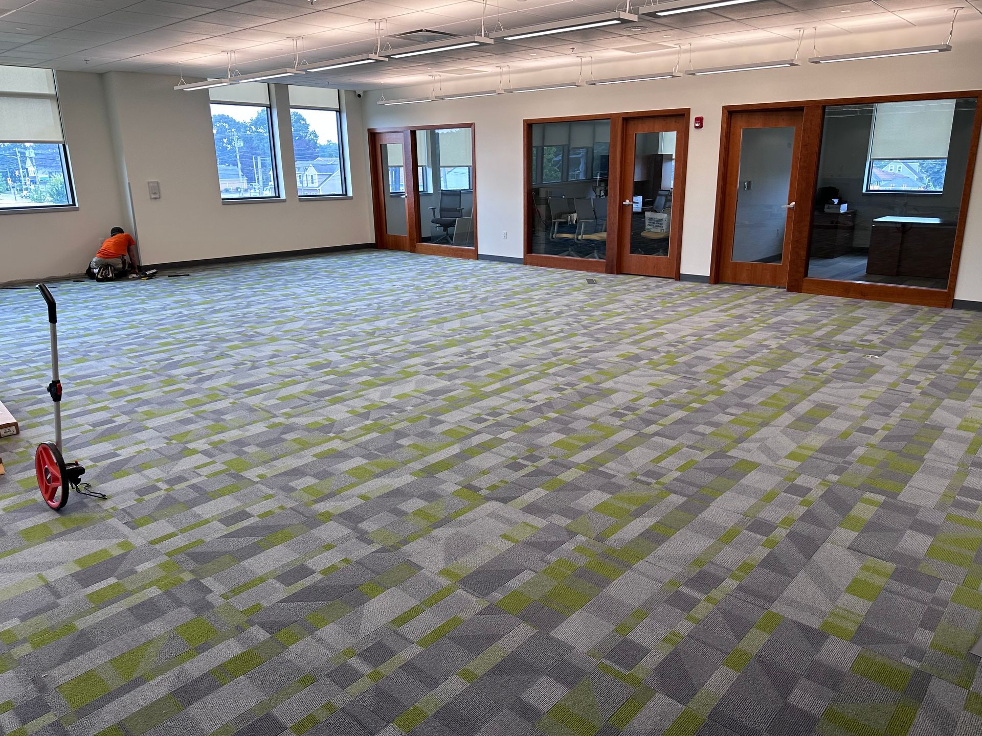 A large room with a green and gray carpet and a wheelbarrow in the middle.
