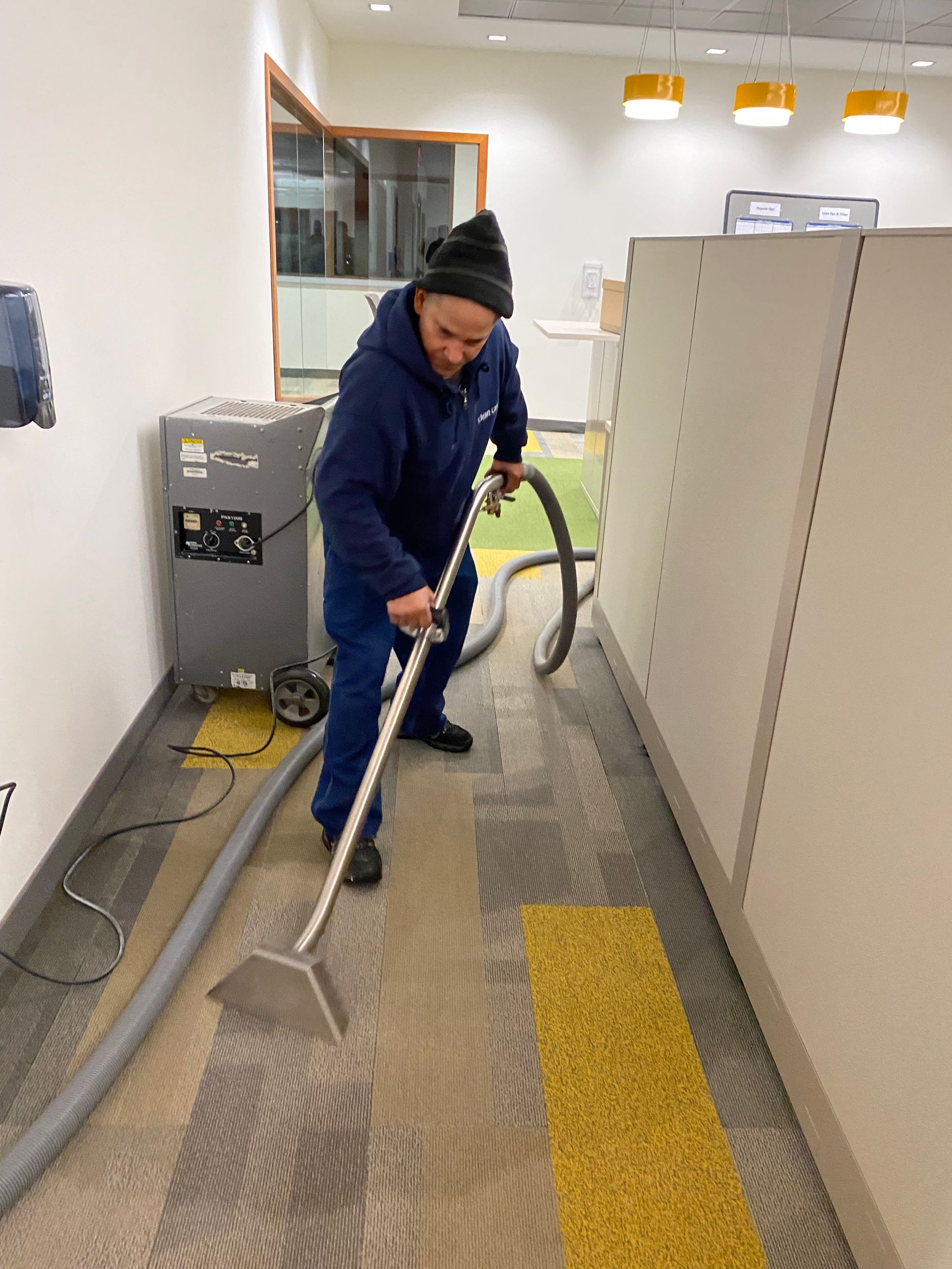 A man is using a vacuum cleaner to clean a carpet in an office.