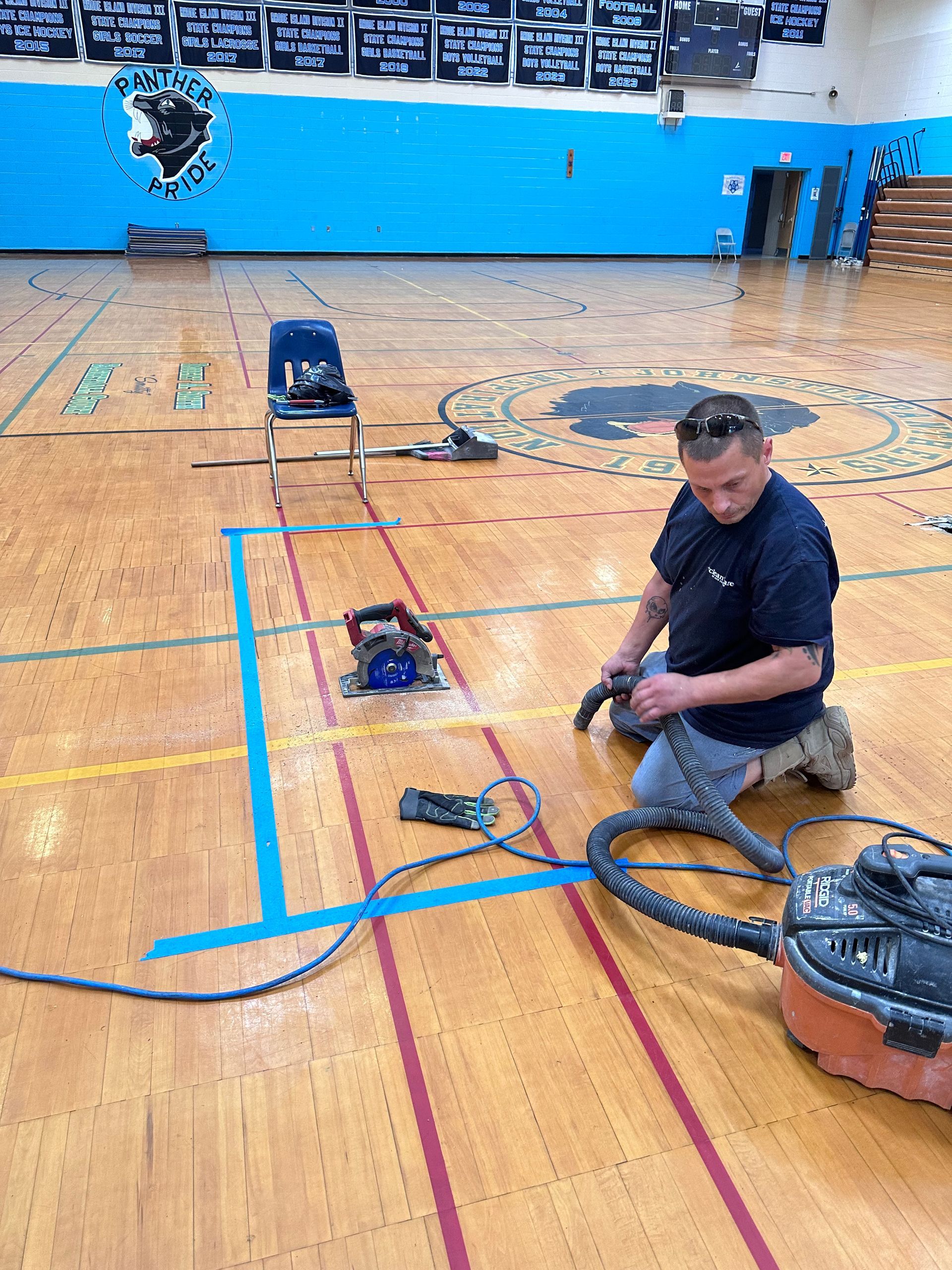A man is kneeling down in a gym with a vacuum cleaner.