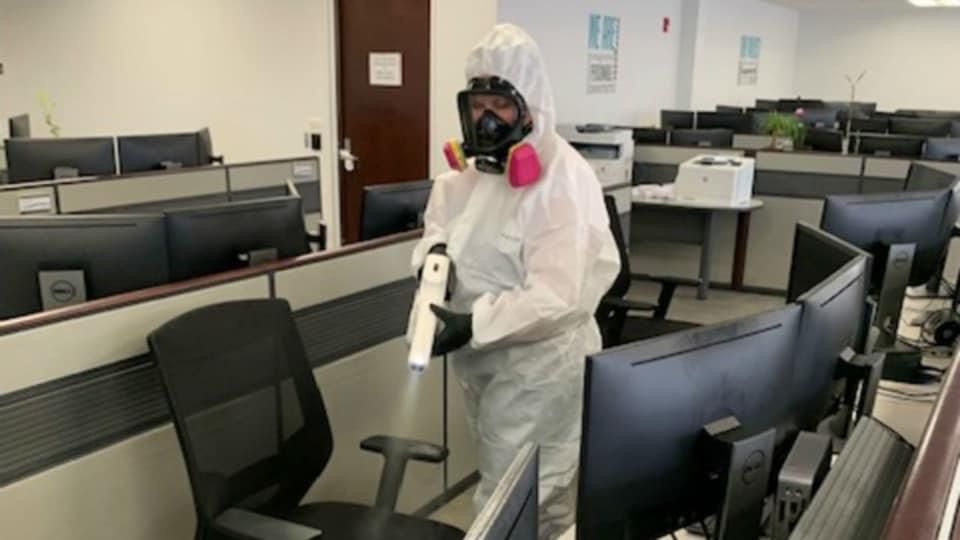 A man in a protective suit is spraying disinfectant in an office.