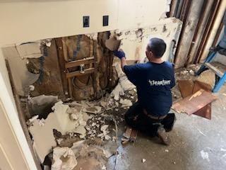 A man is kneeling down in a messy room.