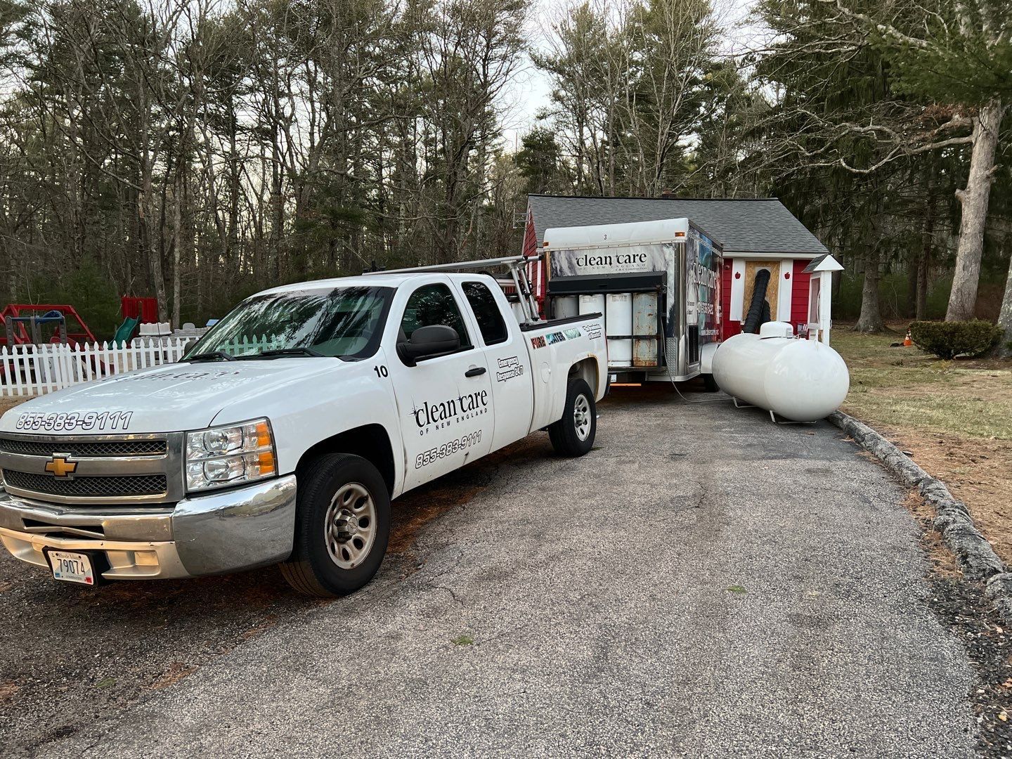 A white truck with a trailer attached to it is parked in front of a house.