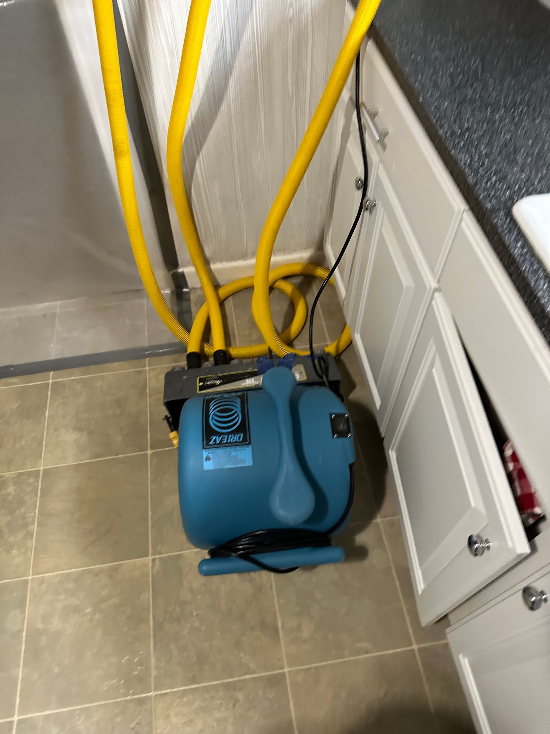 A blue vacuum cleaner is sitting on a tiled floor in a kitchen.
