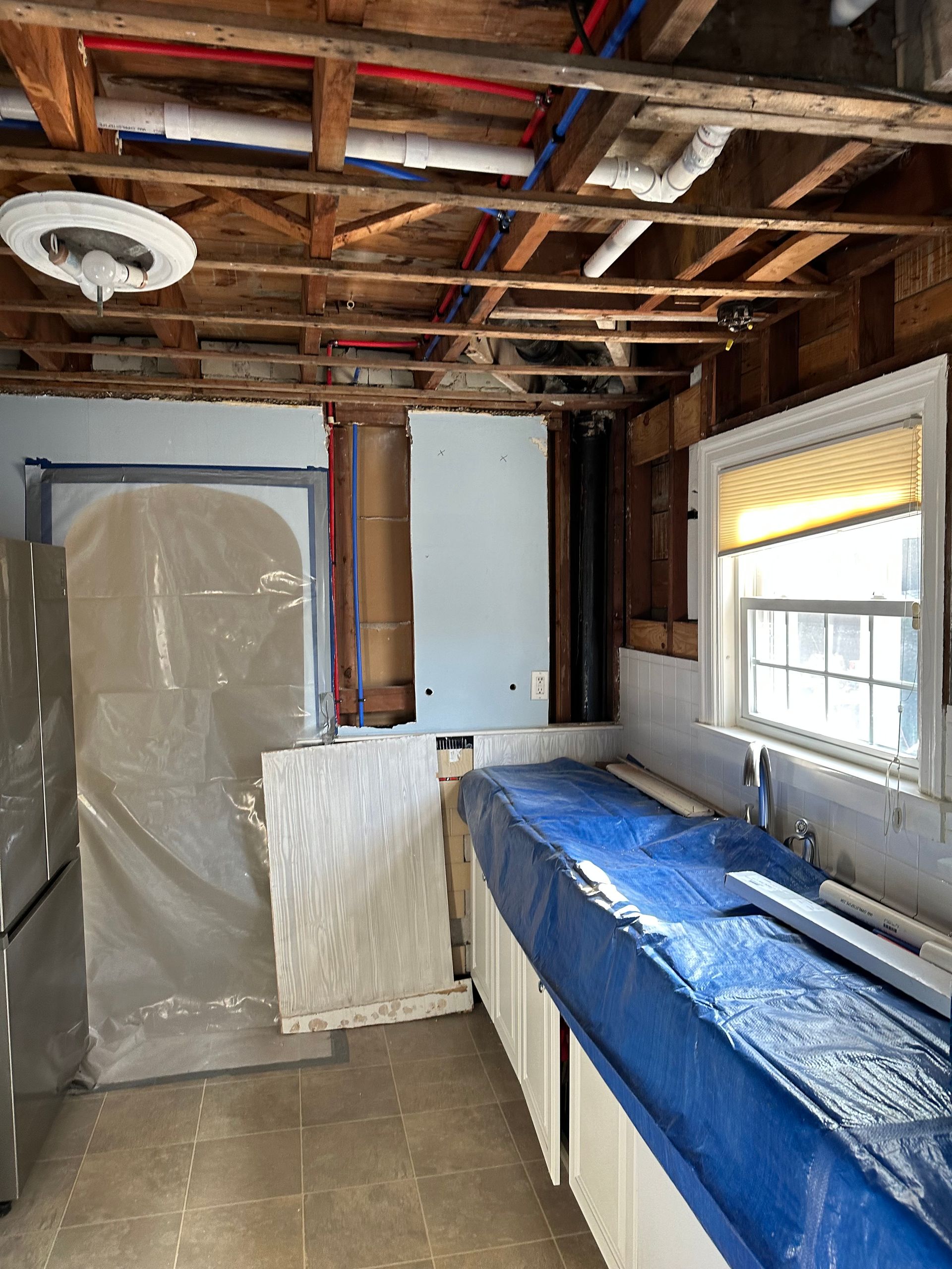 A kitchen with a blue tarp on the counter and a window.