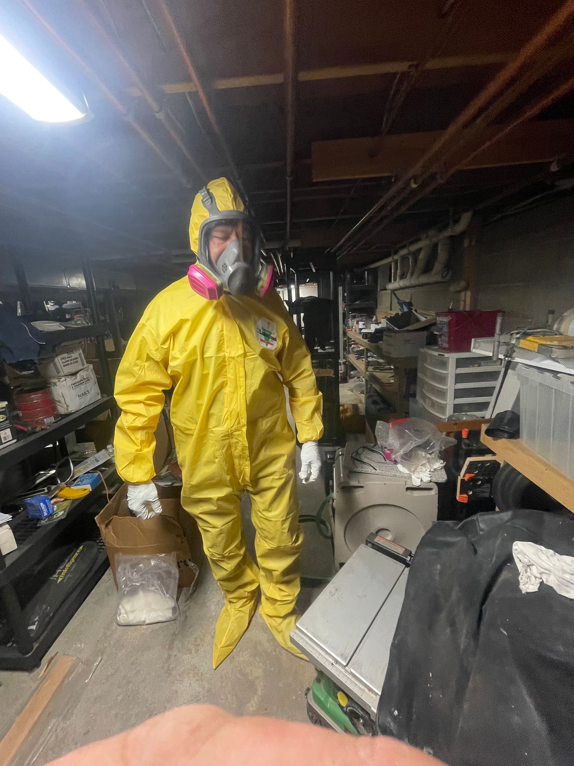 A man in a yellow protective suit is standing in a messy room.