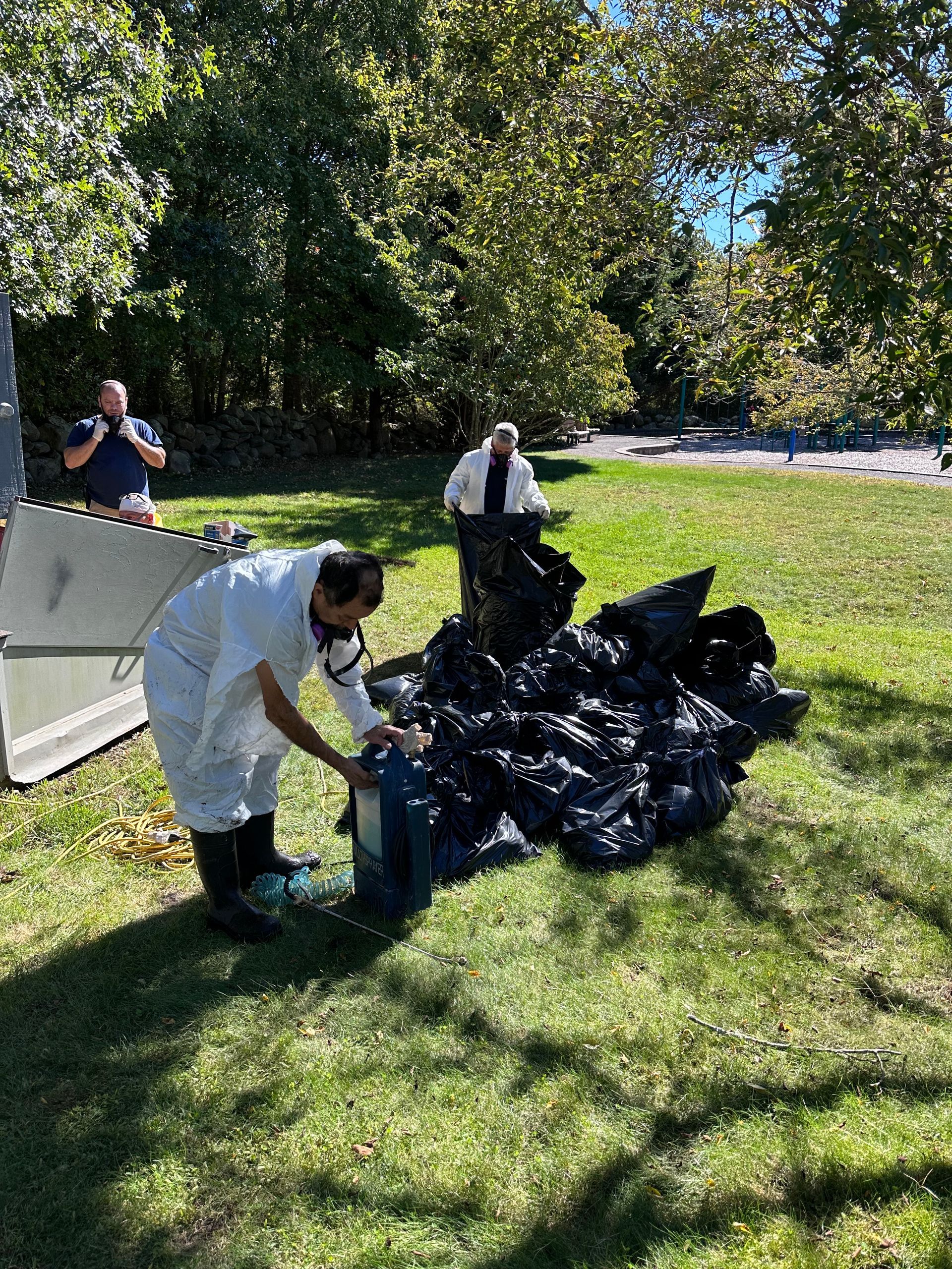A man is standing next to a pile of trash bags in a park.