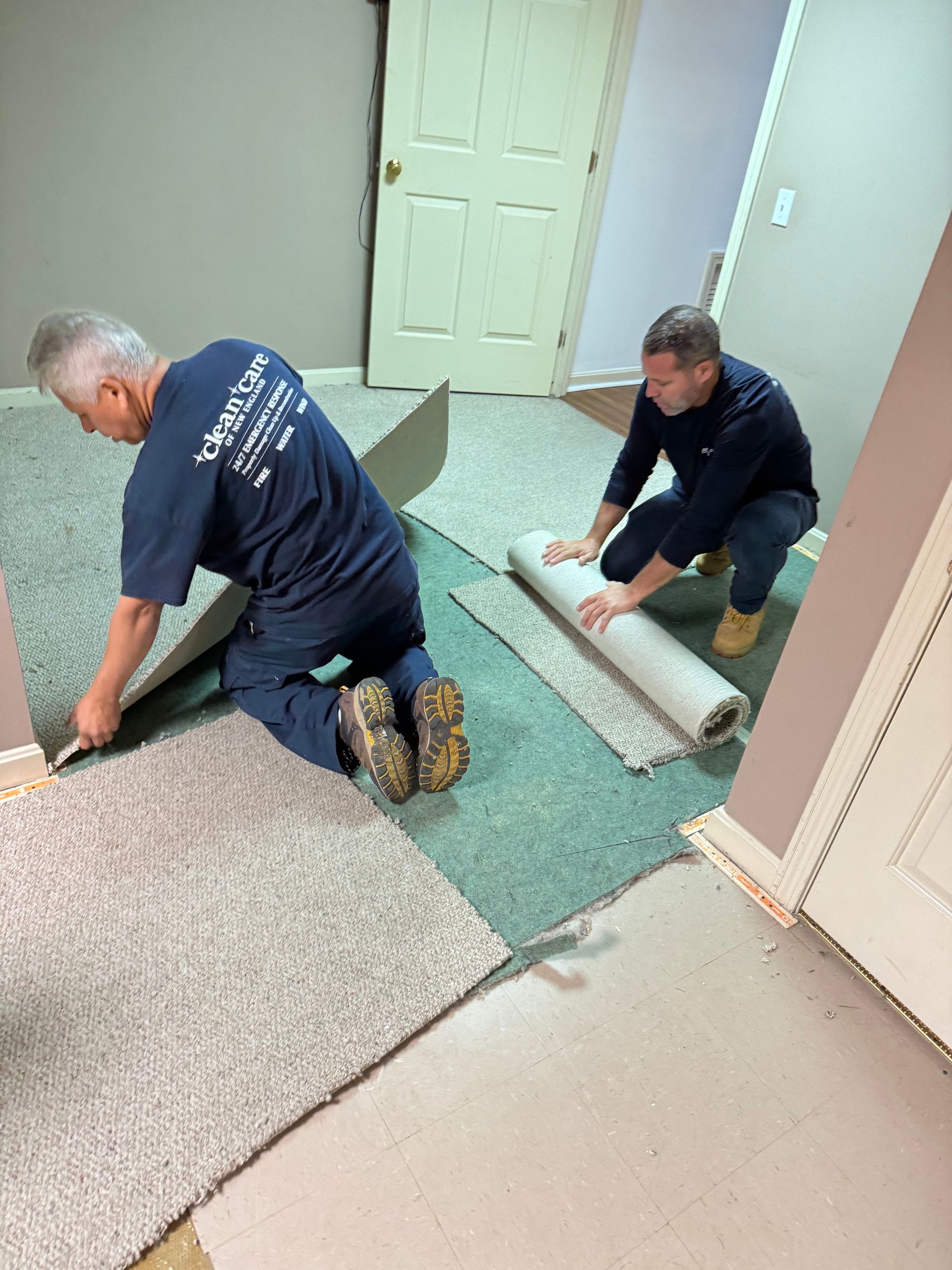 Two men are working on a carpet in a room.