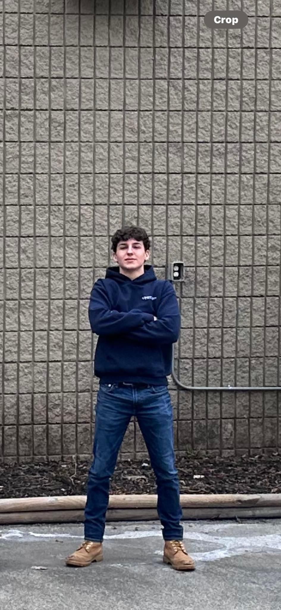 A young man is standing in front of a brick wall with his arms crossed.