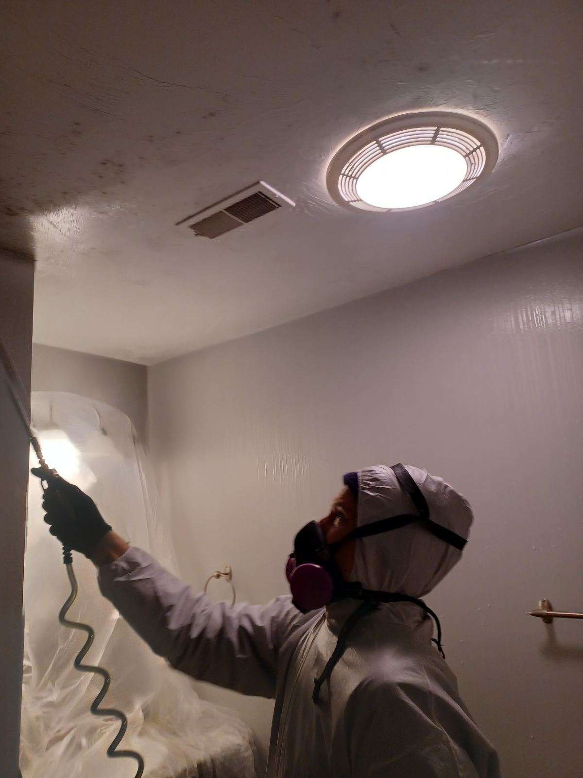 A man wearing a gas mask is spraying a wall in a bathroom.