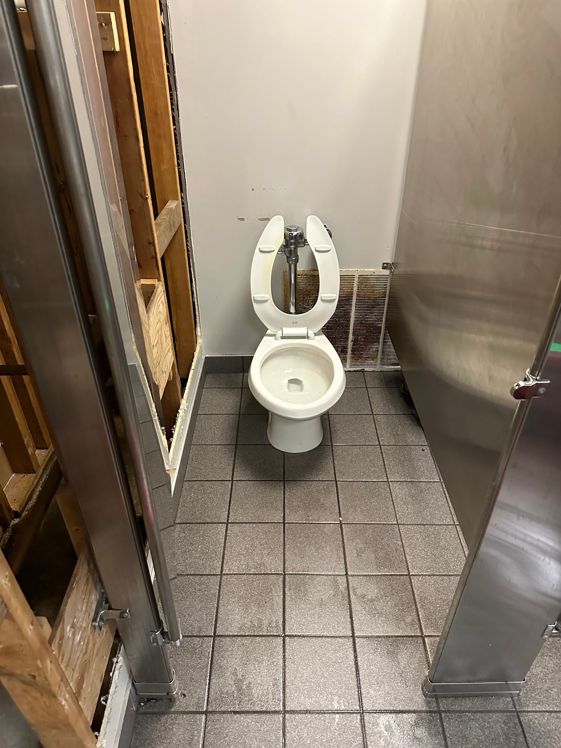 A toilet is sitting on a tiled floor in a bathroom next to a refrigerator.