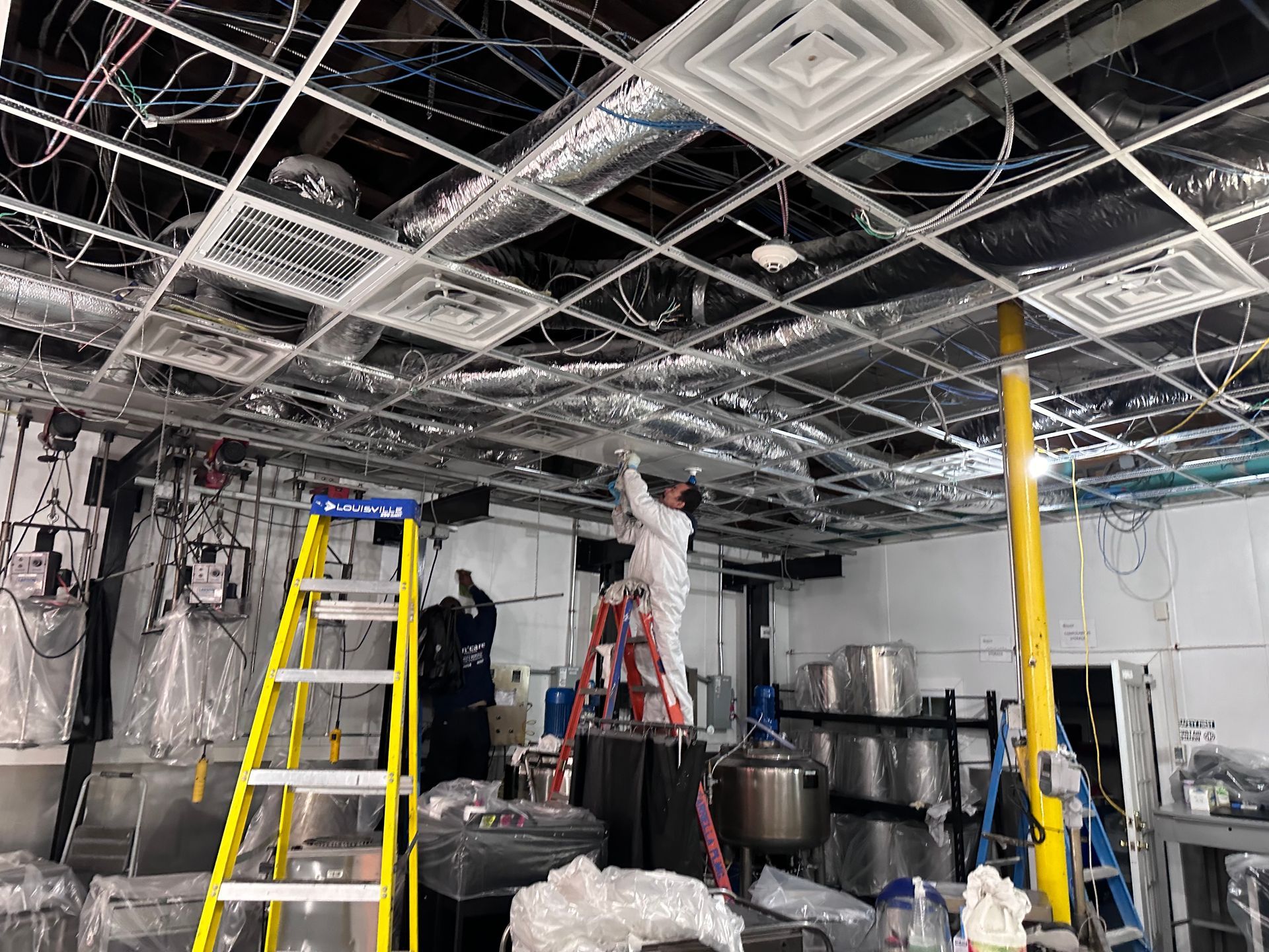 A man on a ladder is working on the ceiling of a building.