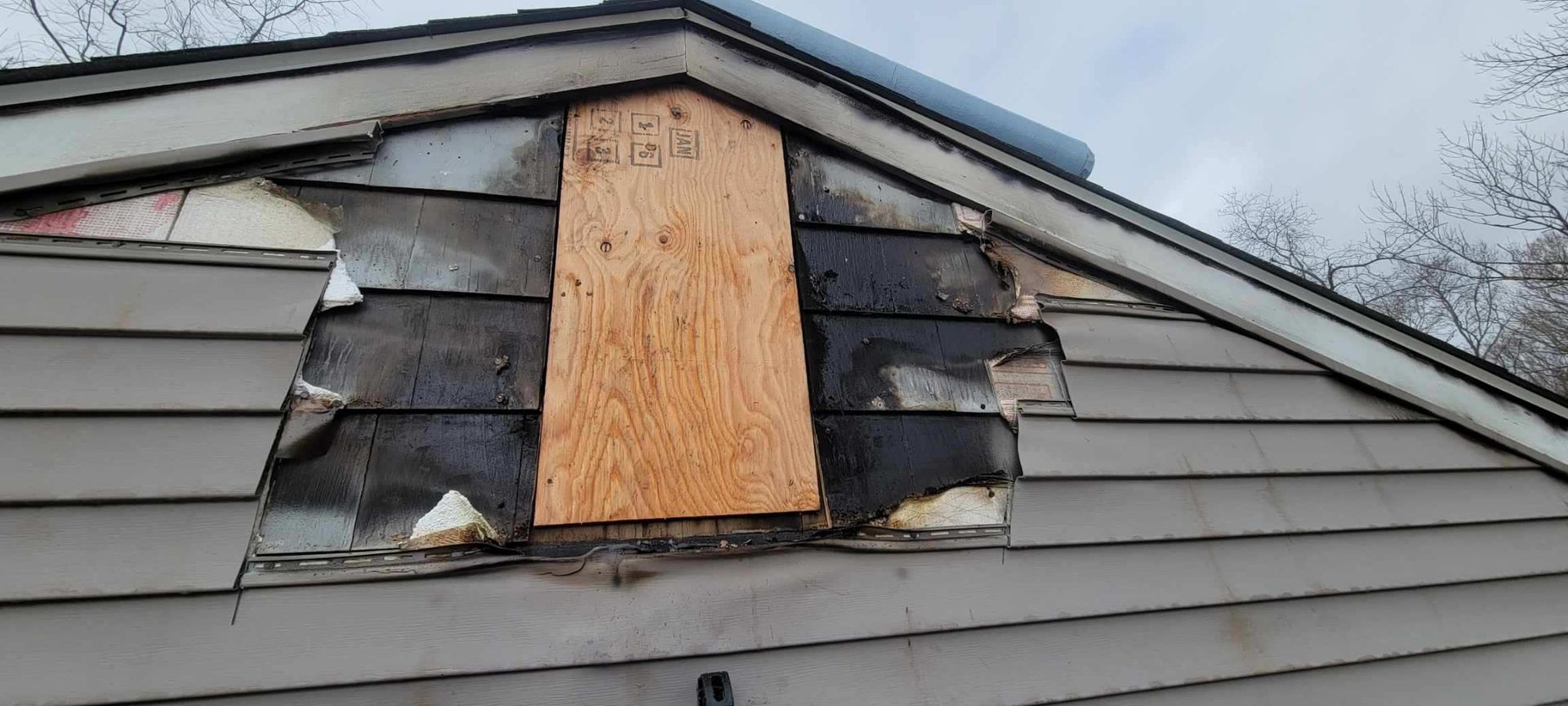 A house with a hole in the roof and a boarded in window.