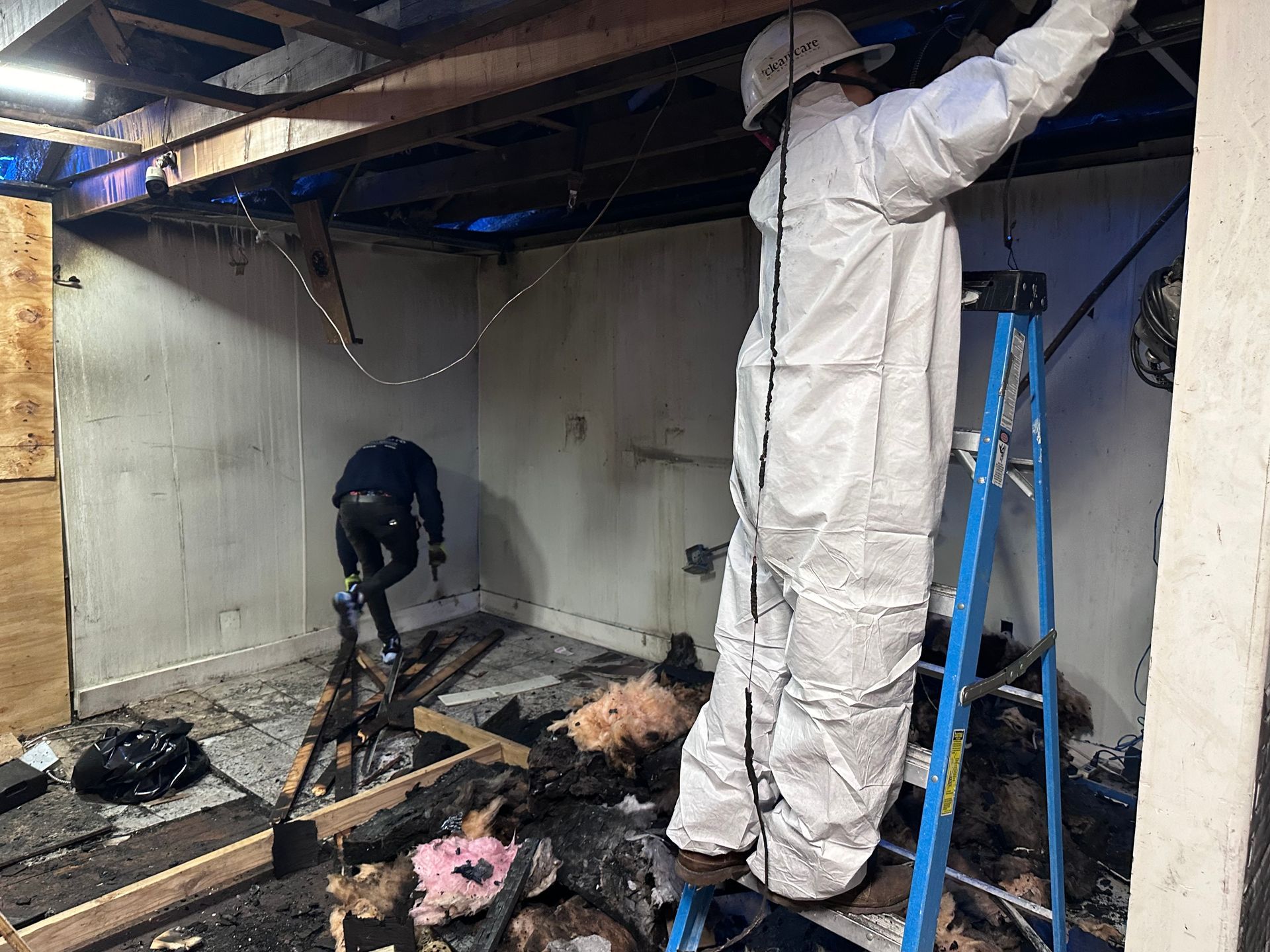 A man in a protective suit is standing on a ladder in a room.