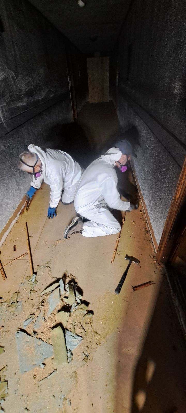 Two people in white suits are working on a wooden floor.
