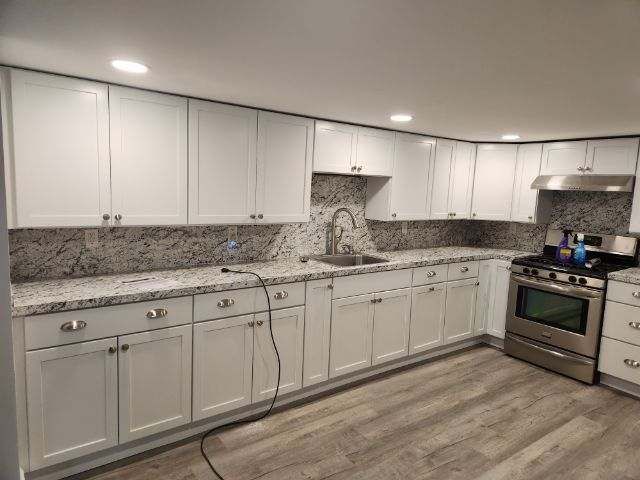 A kitchen with white cabinets , granite counter tops , and stainless steel appliances.