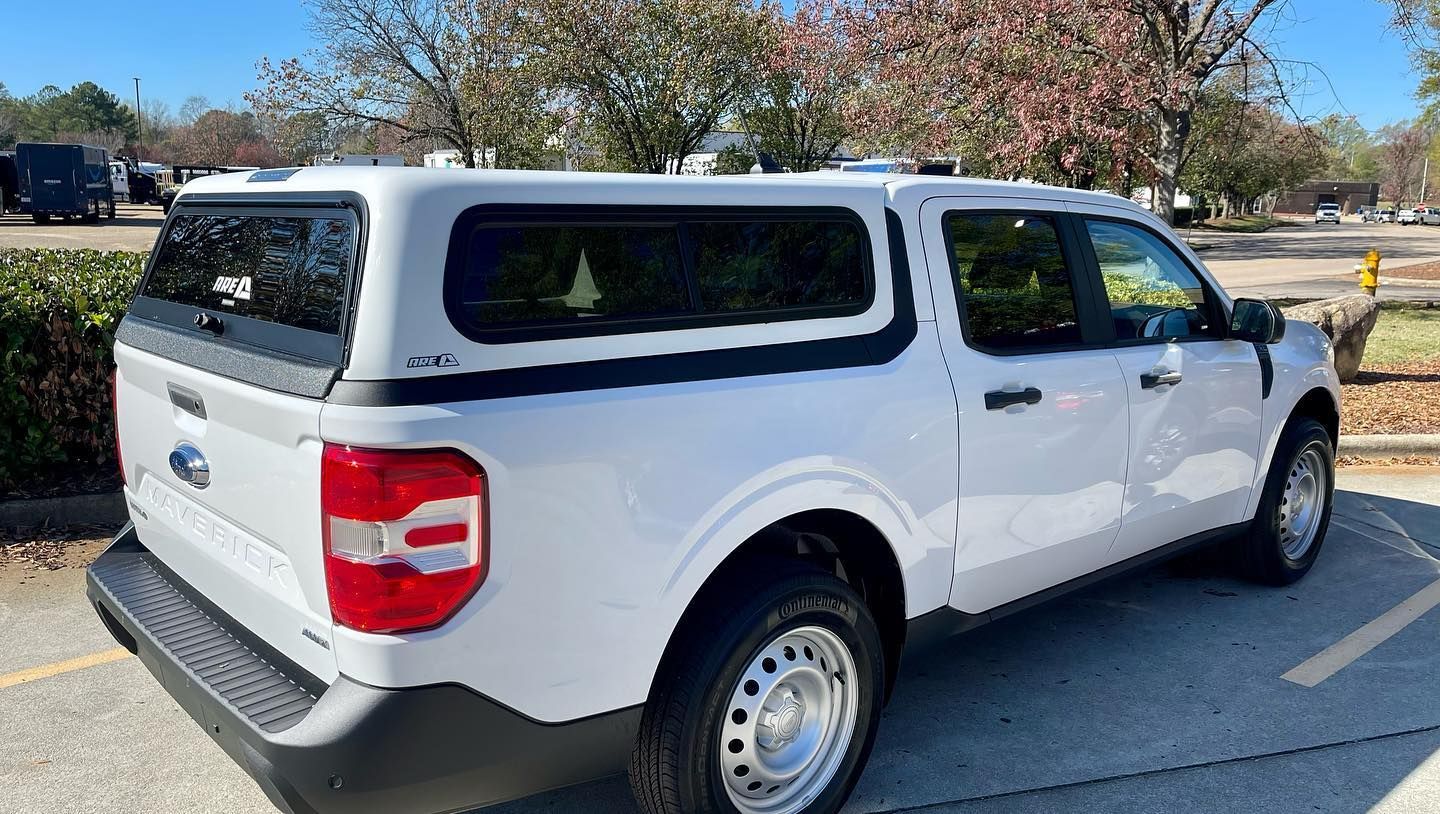 White Ford Maverick truck with a canopy parked in a parking lot on a sunny day.