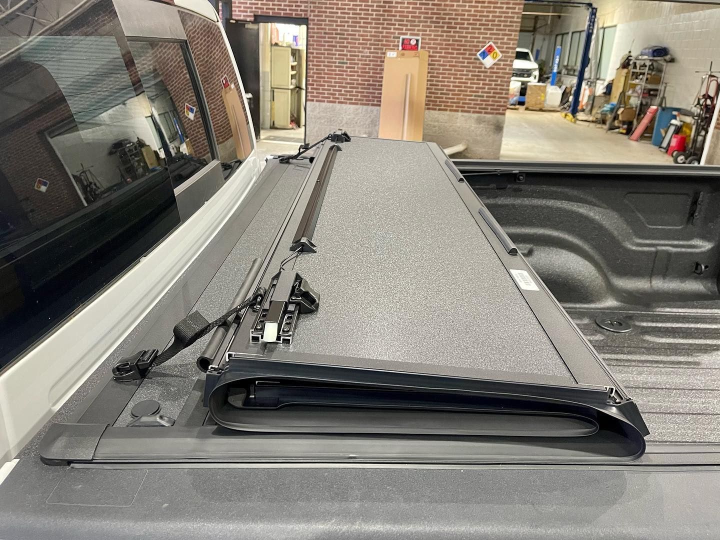 Black, textured tonneau cover on a white pickup truck bed, in a garage setting.
