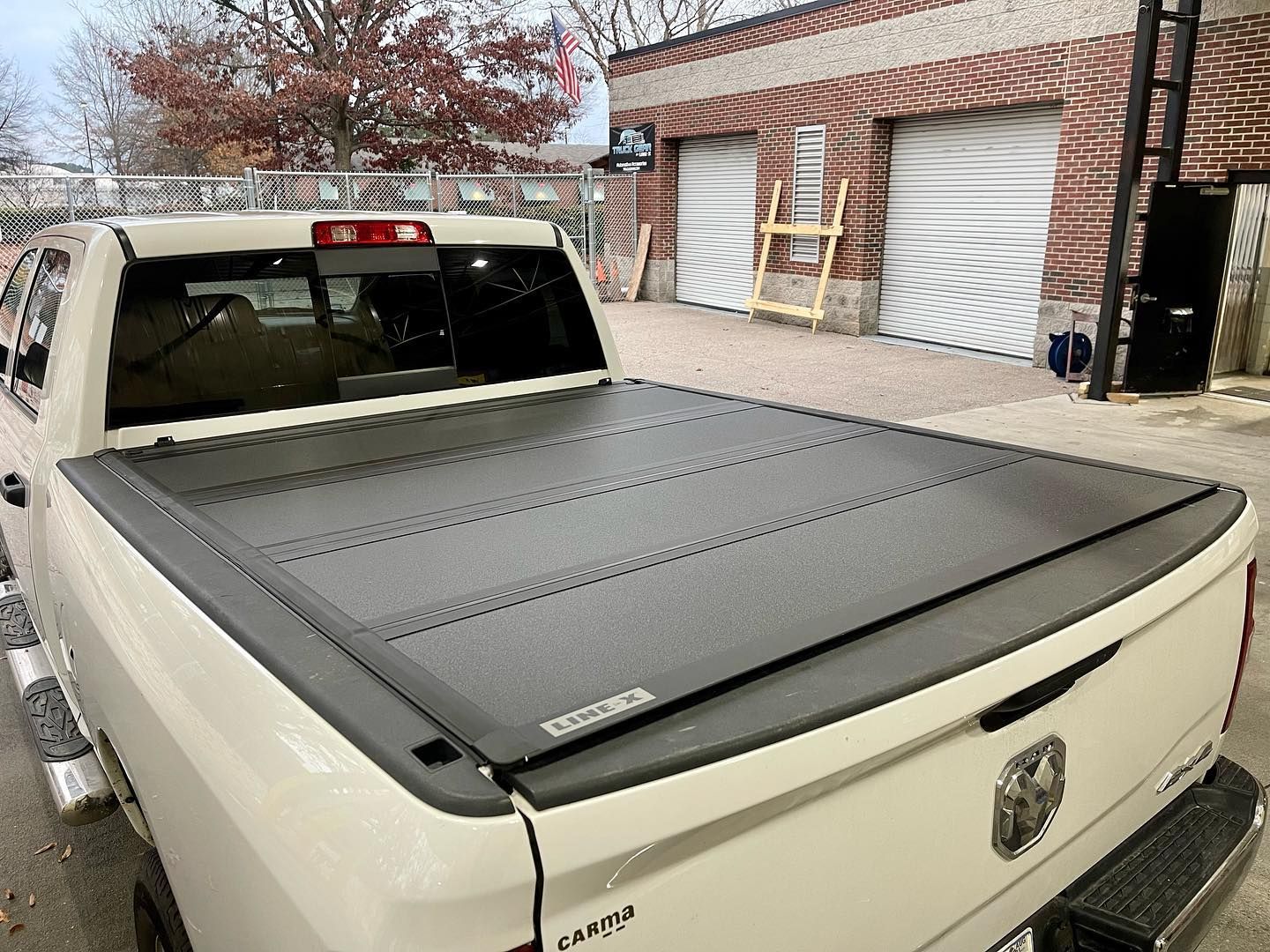 Beige pickup truck with black bed cover parked outside a brick building.