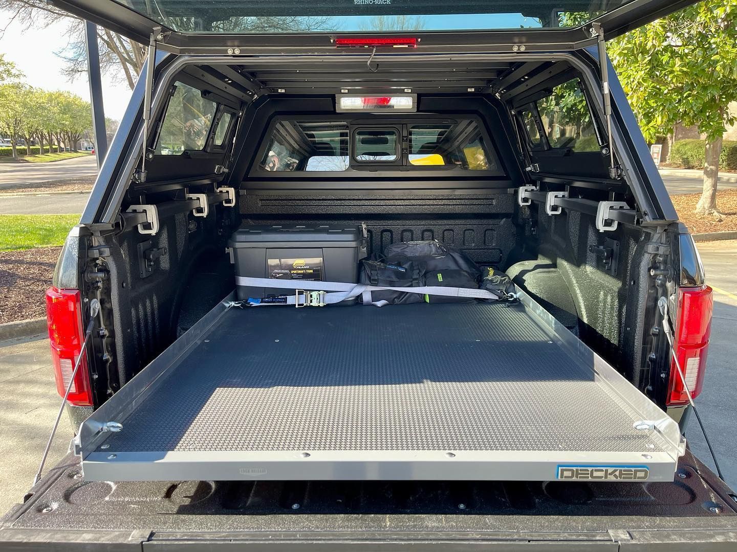 Black pickup truck bed with a slide-out tray and cap open, containing storage and equipment.