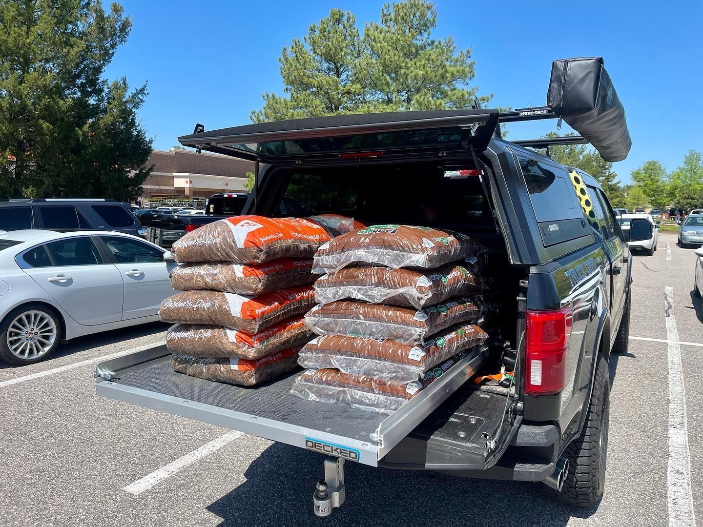 Truck bed loaded with bags of soil, parked in a parking lot on a sunny day.